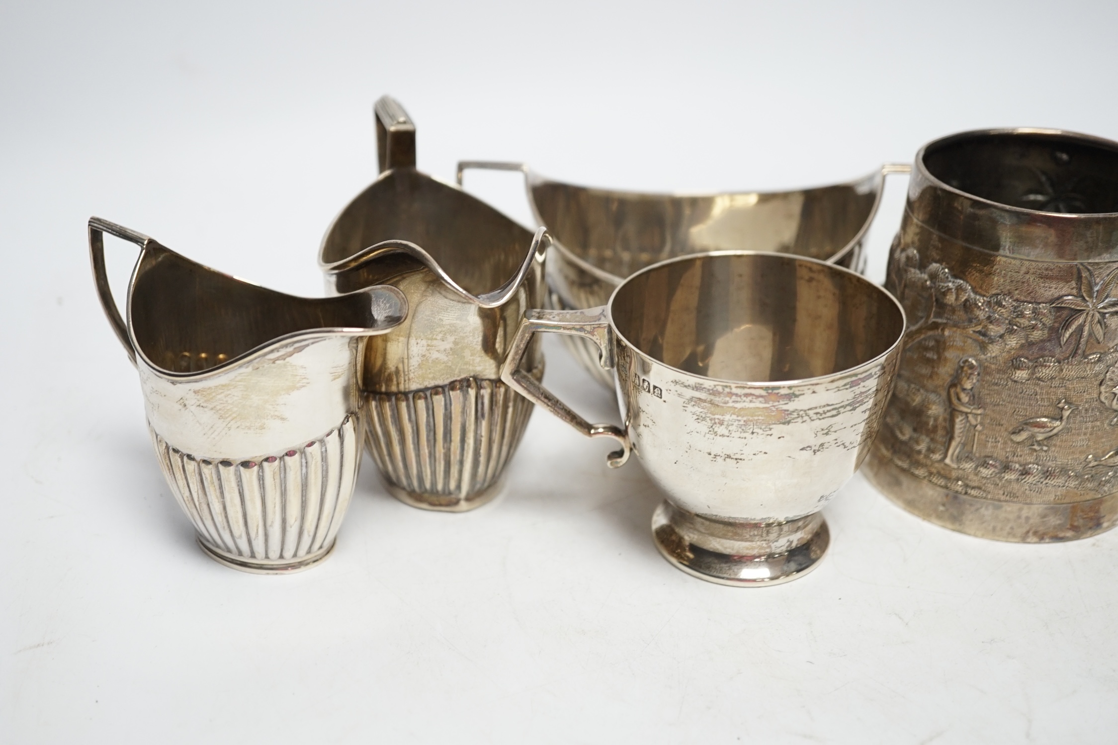 Two early 20th century demi-fluted silver cream jugs and a similar sugar bowl, an Irish silver tea cup and an Indian? white metal mug, gross weight 16.7oz. Fair condition.